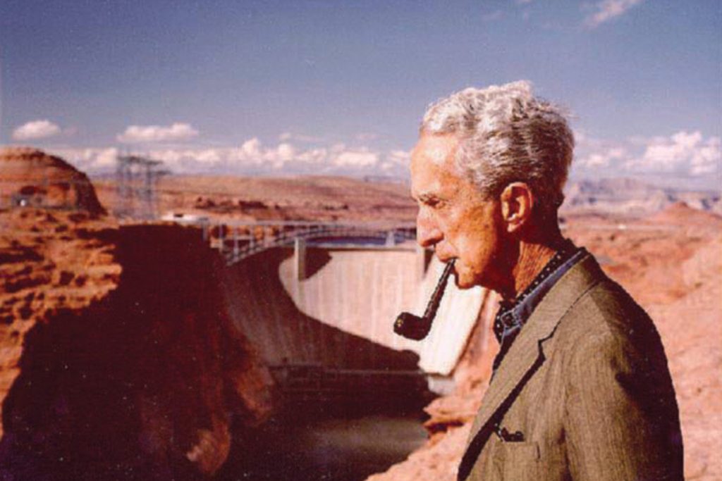 Photo of Norman Rockwell overlooking the Glen Canyon Dam while smoking a pipe.