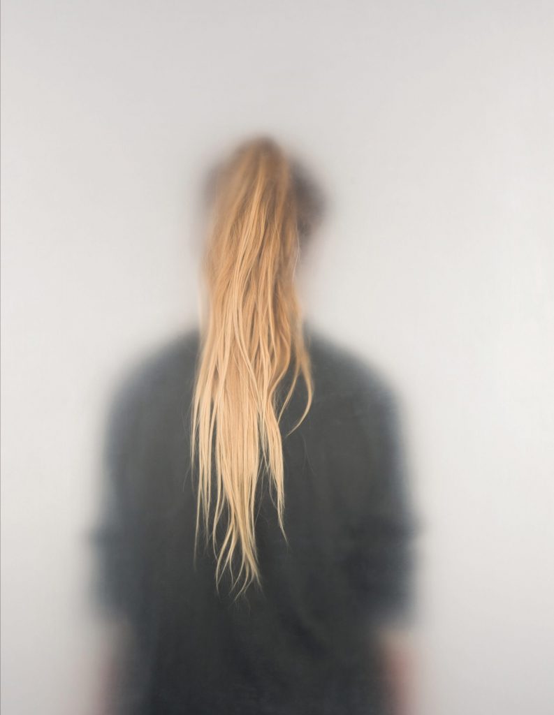 Artistic photo of a woman turned around through a cloudy vellum.