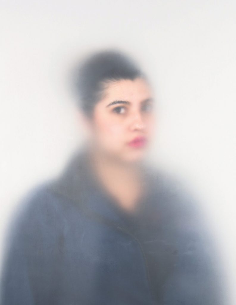 Artistic photo of a woman looking at the viewer through a cloudy vellum.