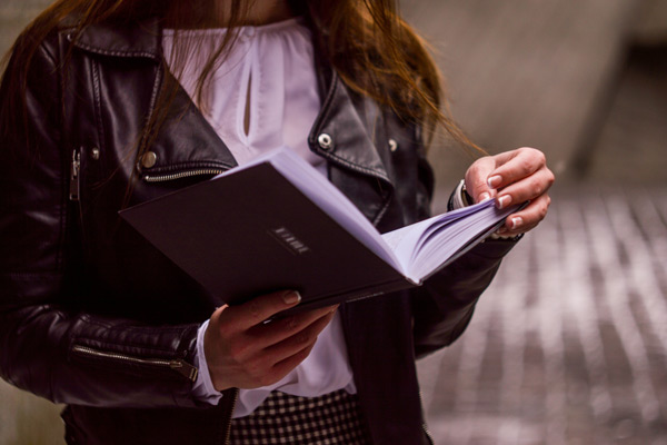 Women in leather jacket holding open book.