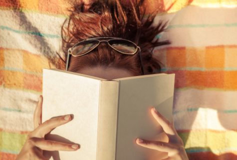 Woman with sunglasses with book covering her face.