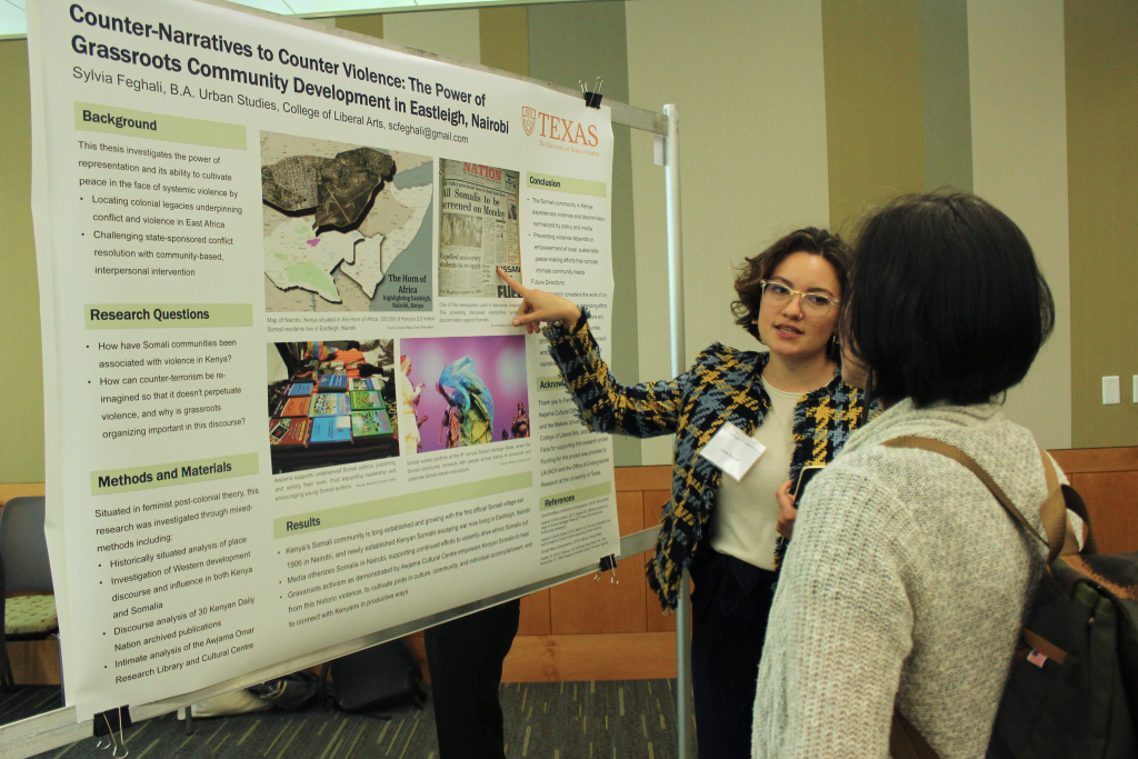 Sylvia Feghali points to her research poster while speaking to a woman. 