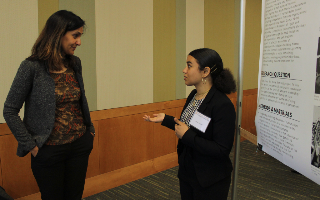 Sarah Ahmed stands in front of her research poster explaining her research. 