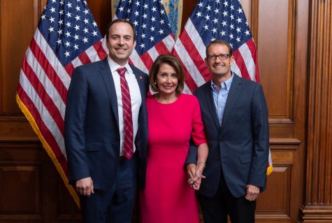 Rep. Lance Gooden, Speaker Nancy Pelosi, and Professor Sean Theriault during Gooden's swearing-in ceremony with three American flags and wooden panel walls as background.