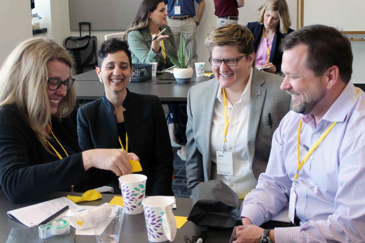 A group of four people with yellow lanyards around their necks laughing and working together during a Design Thinking workshop.
