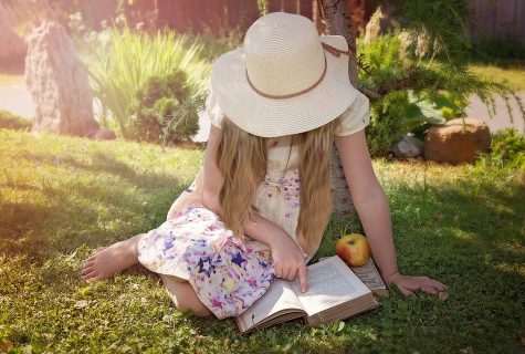 Woman sitting on grass while reading book.