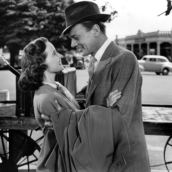 A black and white still from a movie with a man and woman closely talking.
