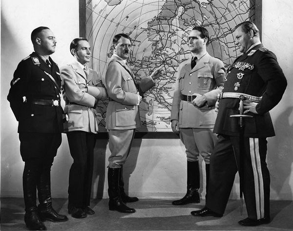 A black and white still showing Nazis gathered around a map of Europe.