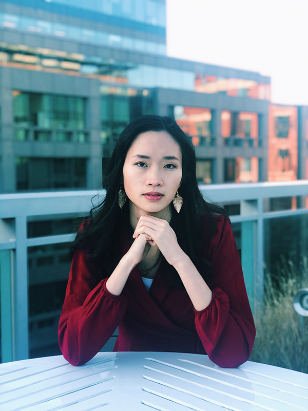 Margaret Siu sits with a contemplative look on her face, with her hands clasped under her chin. 