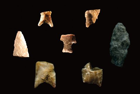 various pieces of arrowheads made of stone on a black background with a scale of 0-2cm at the bottom