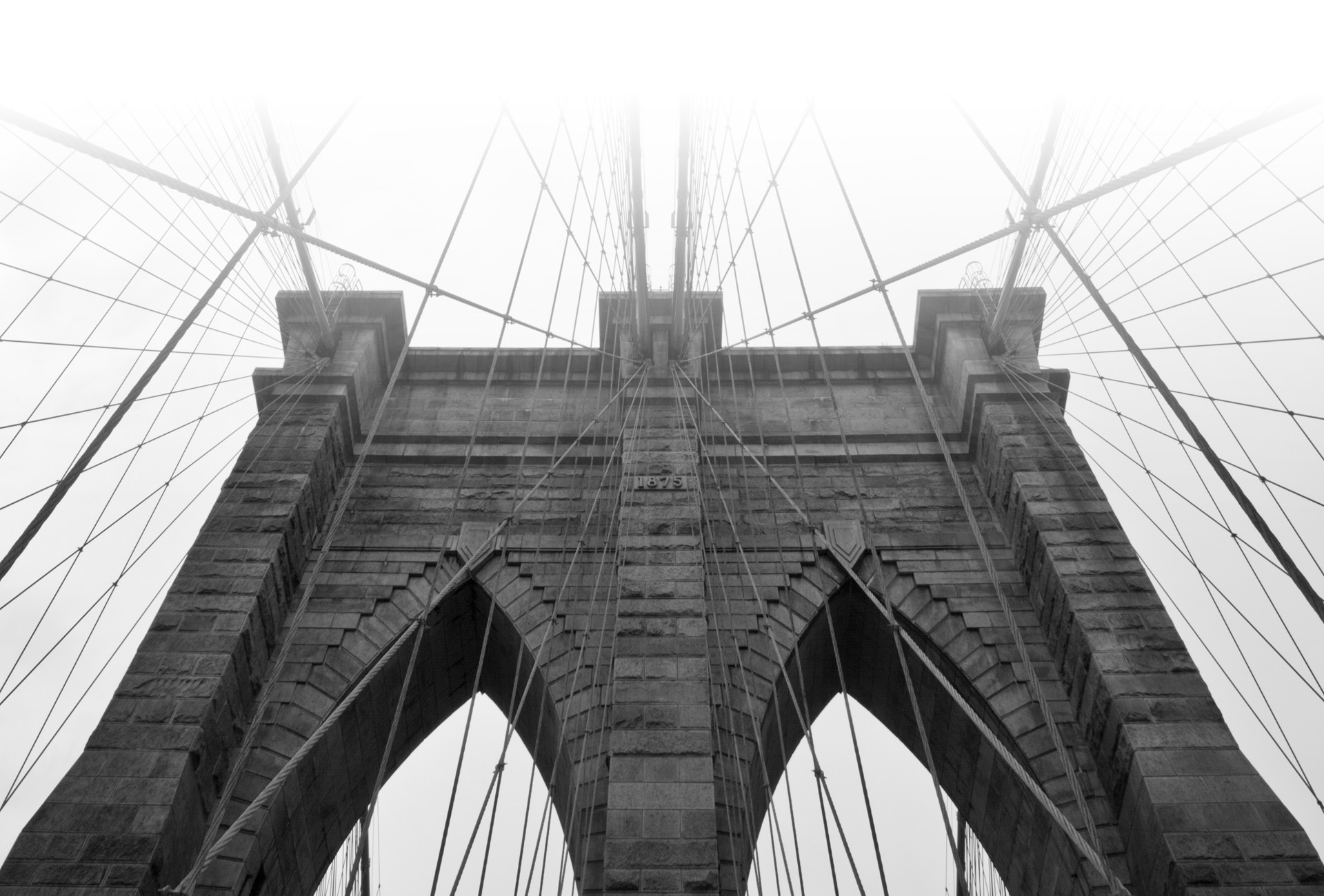 Black and white photo of the Brooklyn Bridge shrouded in a white fog.