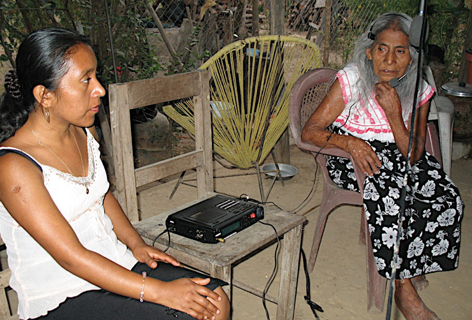 A young woman speaking to an elderly woman. The older woman speaks into a microphone recorder.
