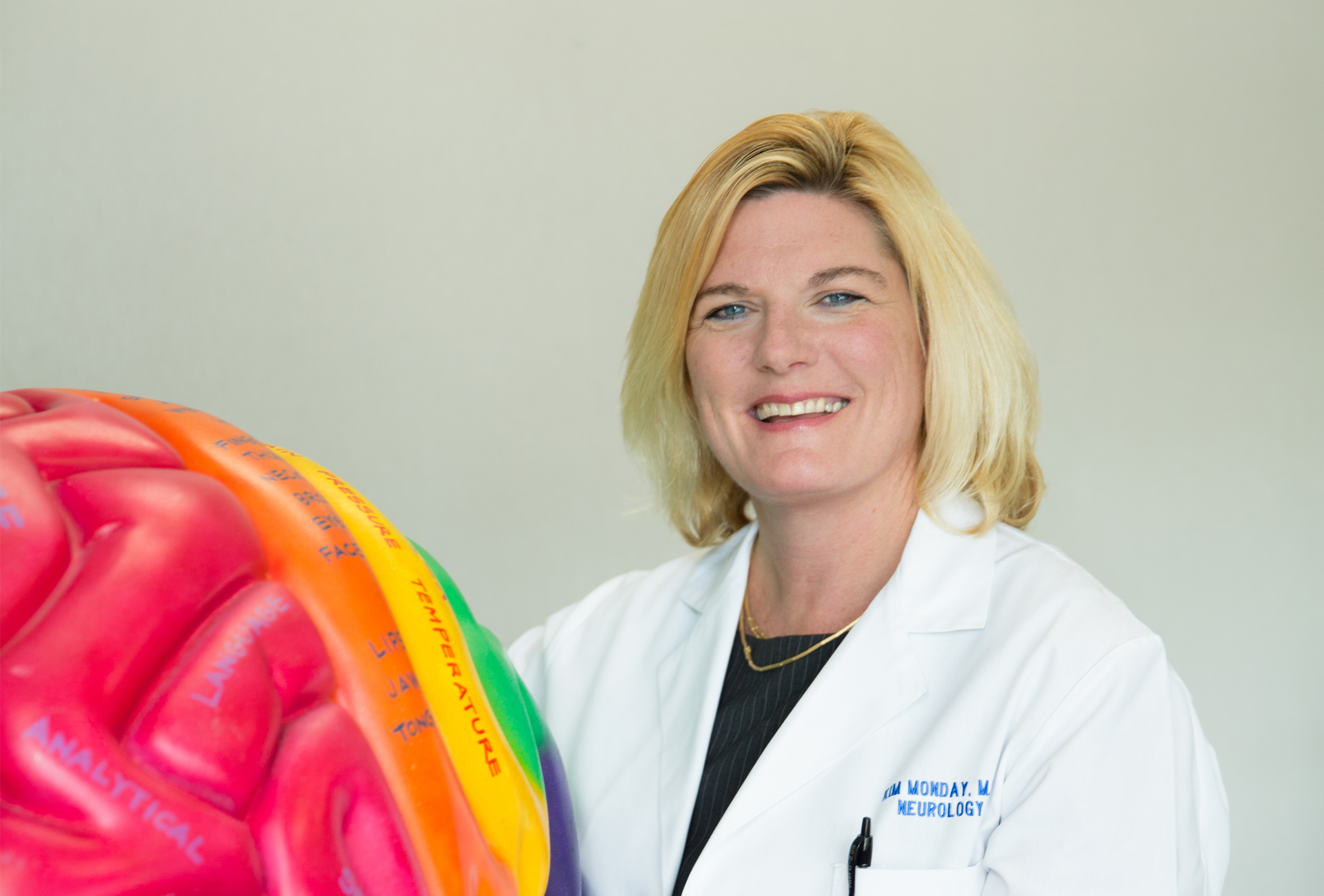 Portrait of Dr. Kimberly Monday standing next to a colorful plastic model of a brain.