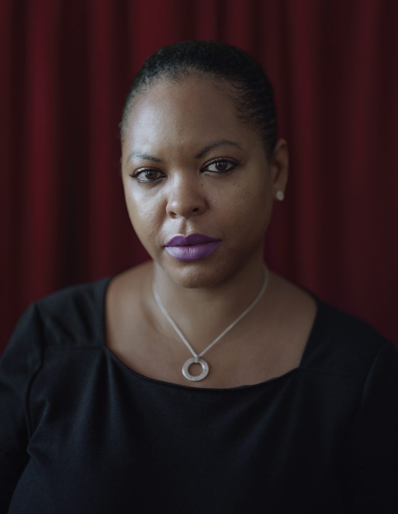 Portrait of Simone Browne against a red curtain.