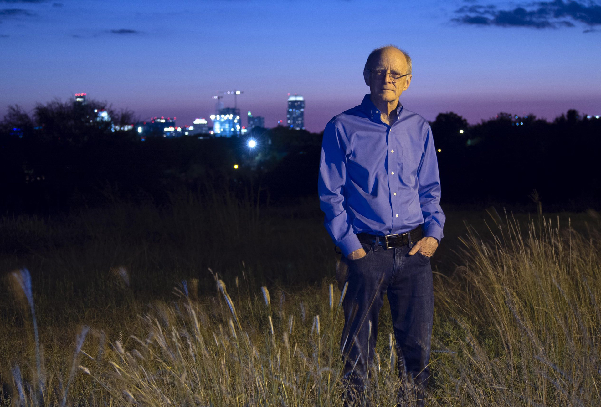 Jamie Pennebaker stands in a field at sunset with cityscape in background.