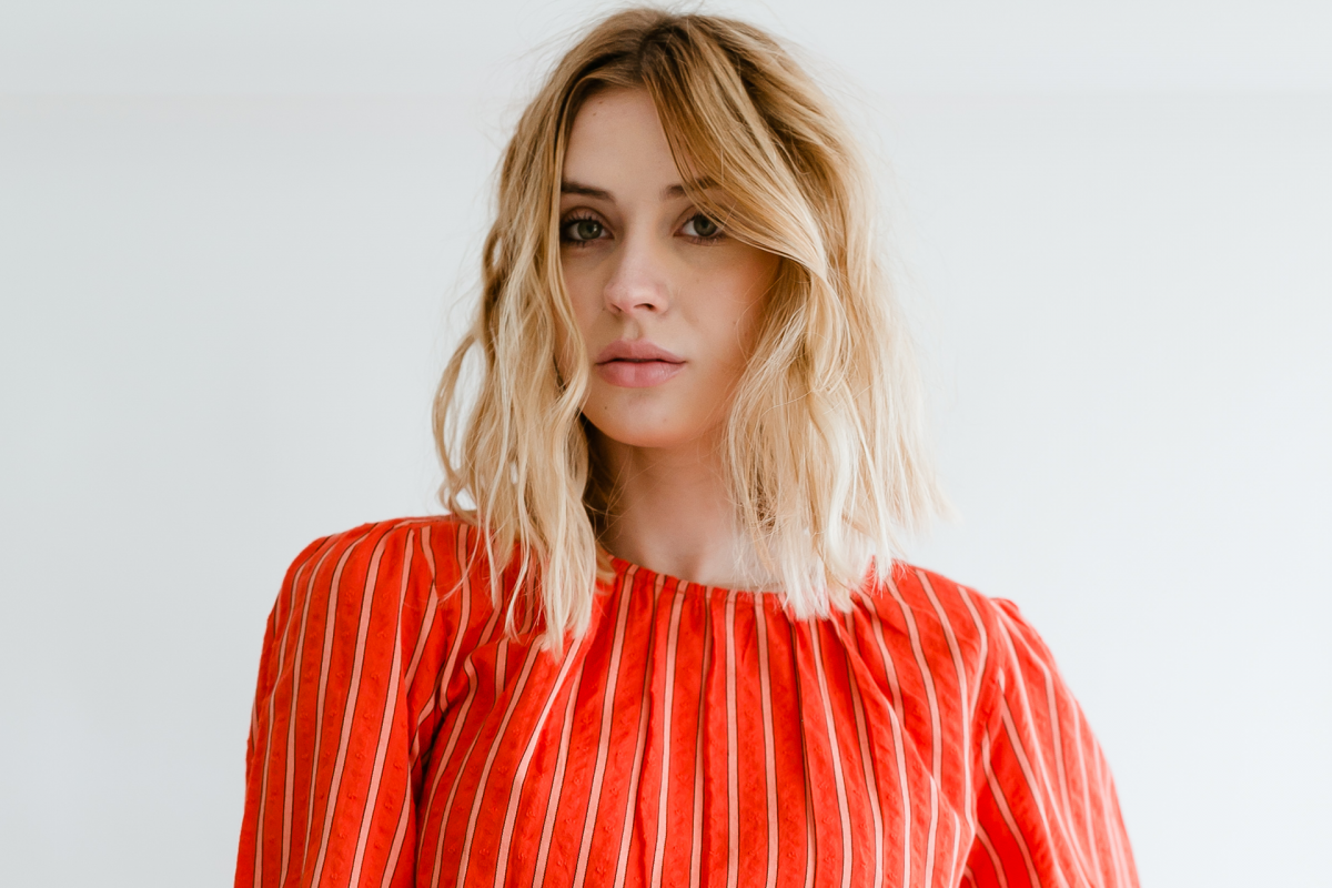 Anna Cash wears a striped red shirt and looks into the camera with a serious expression on her face.