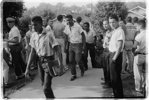 Photograph shows a line of African American boys walking through a crowd of white boys during a period of violence related to school integration.