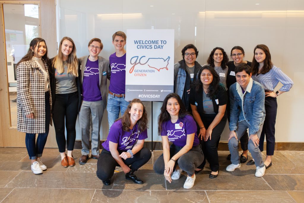 A group shot of Generation Citizen volunteers including Rodriguez. There is a sign with the organization's logo and the words 'Welcome to Civics Day.'