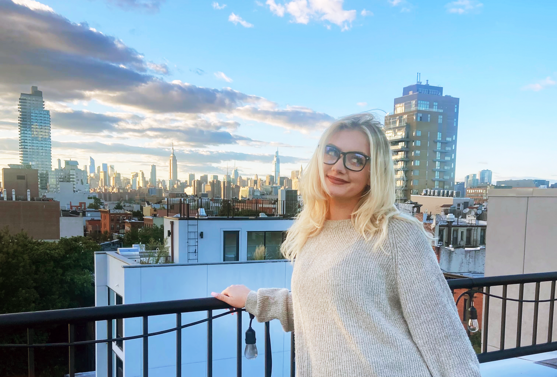 Hannah Hayes stands at a railing as the sun sets over the New York City skyline.
