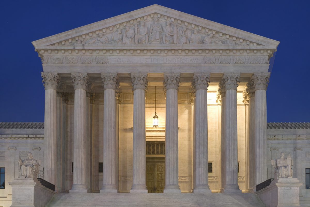 The Supreme Court of the United States at night, with lights glowing from within the columns of the building.