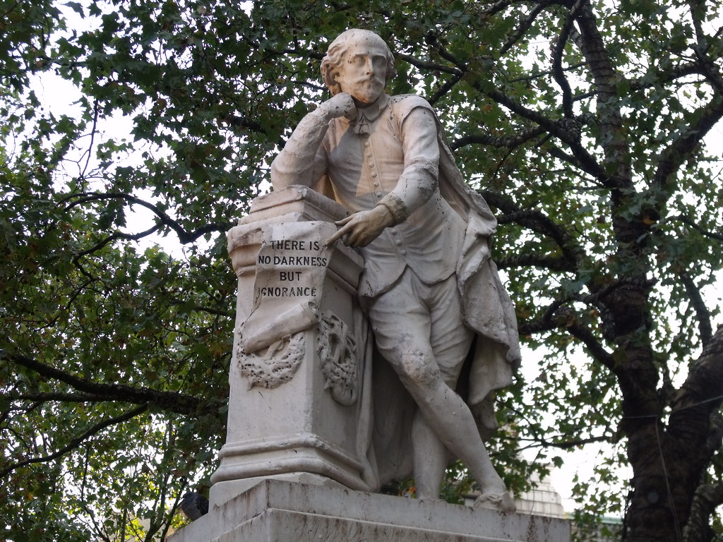 A statue of William Shakespeare leaning against a column, holding a scroll that reads "There is no darkness but ignorance."
