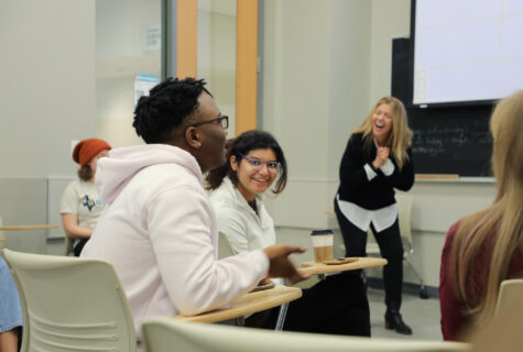 Students talking in American Sign Language in the foreground with instructor in the background during an ASL class